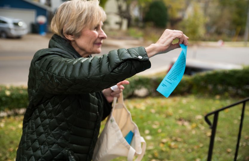 After applying tape to the top of the note, Bate reaches out to place the note on a neighborhood door.